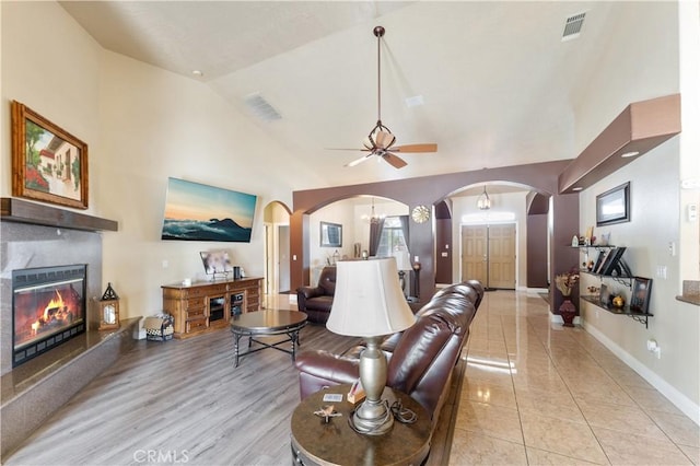 living room featuring a fireplace, ceiling fan with notable chandelier, light tile patterned floors, and vaulted ceiling