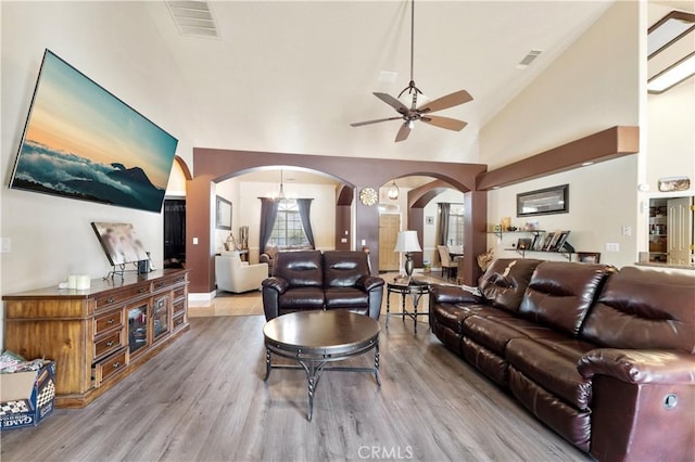 living room featuring ceiling fan with notable chandelier, light hardwood / wood-style floors, and high vaulted ceiling