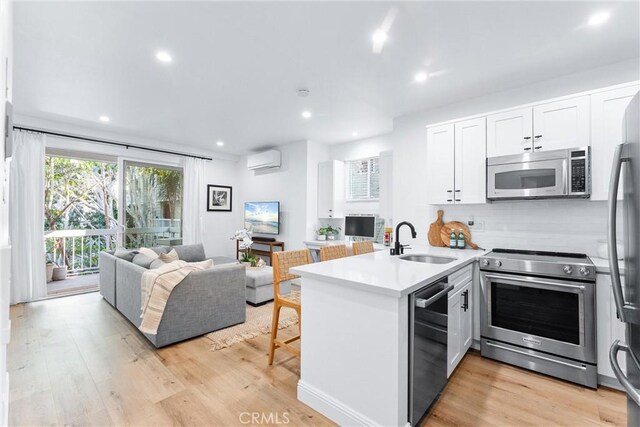 kitchen with kitchen peninsula, sink, white cabinetry, a wall mounted air conditioner, and appliances with stainless steel finishes