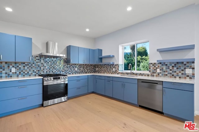 kitchen featuring appliances with stainless steel finishes, wall chimney exhaust hood, tasteful backsplash, sink, and blue cabinets