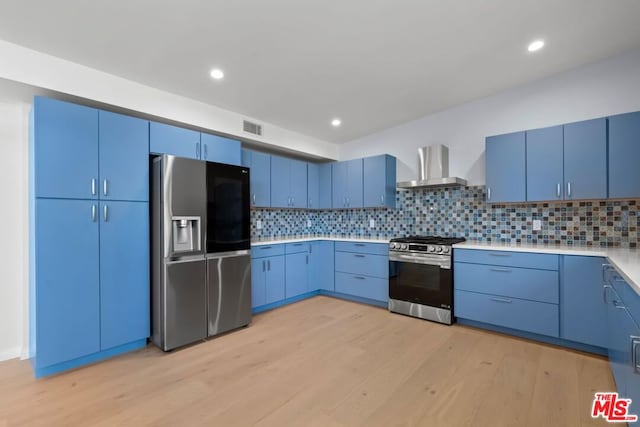 kitchen with backsplash, wall chimney range hood, stainless steel appliances, and blue cabinets