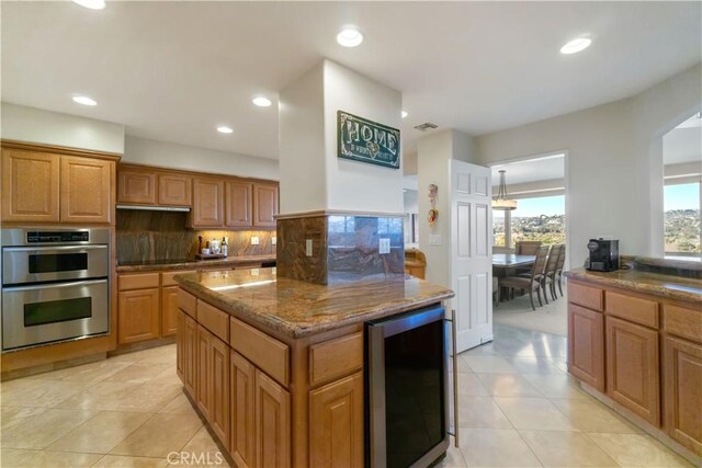 kitchen featuring beverage cooler, a center island, light tile patterned floors, stainless steel double oven, and backsplash