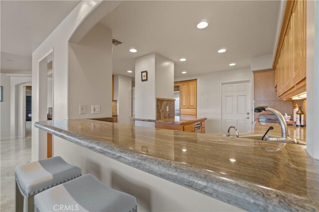 kitchen featuring sink, decorative backsplash, light stone counters, and kitchen peninsula