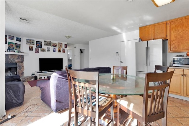 dining space featuring a fireplace, light tile patterned flooring, and a textured ceiling