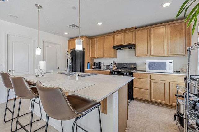 kitchen featuring black appliances, a breakfast bar, an island with sink, and pendant lighting