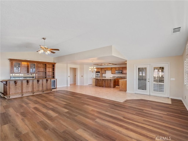 unfurnished living room with ceiling fan with notable chandelier, hardwood / wood-style floors, and vaulted ceiling