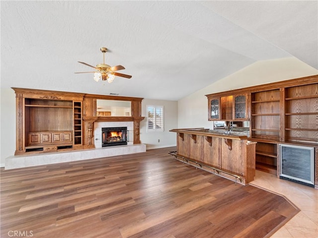 kitchen featuring ceiling fan, vaulted ceiling, hardwood / wood-style floors, a tiled fireplace, and a textured ceiling