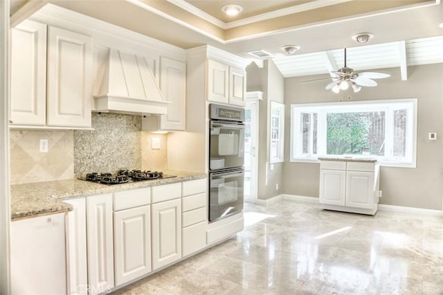 kitchen with multiple ovens, custom exhaust hood, gas stovetop, white cabinets, and light stone counters