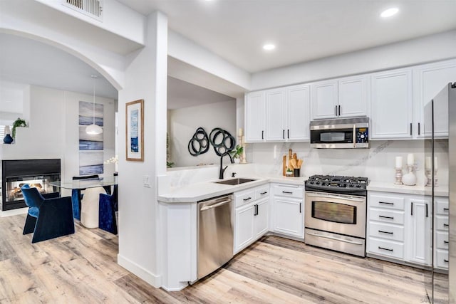 kitchen with appliances with stainless steel finishes, a multi sided fireplace, hanging light fixtures, white cabinets, and sink