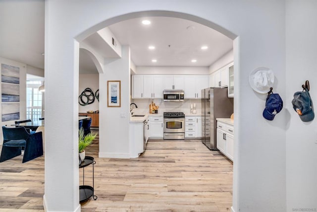 kitchen with light wood-type flooring, appliances with stainless steel finishes, white cabinetry, and sink