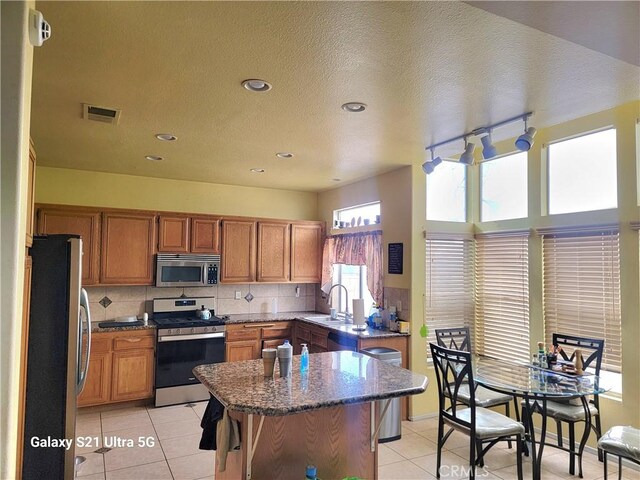 kitchen with light tile patterned floors, sink, backsplash, stainless steel appliances, and dark stone counters