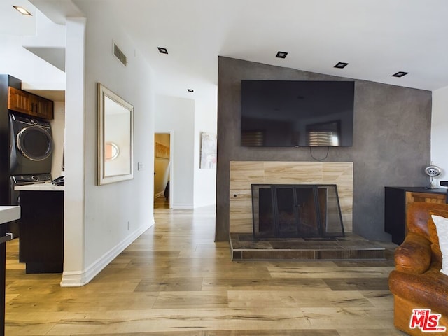 living room featuring stacked washer / dryer, a fireplace, and light hardwood / wood-style flooring