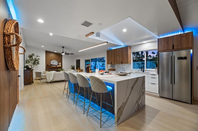 kitchen with a kitchen island, backsplash, light hardwood / wood-style flooring, high end refrigerator, and a breakfast bar area