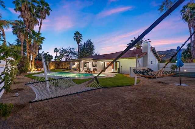 back house at dusk featuring a lawn, a patio, and a fenced in pool