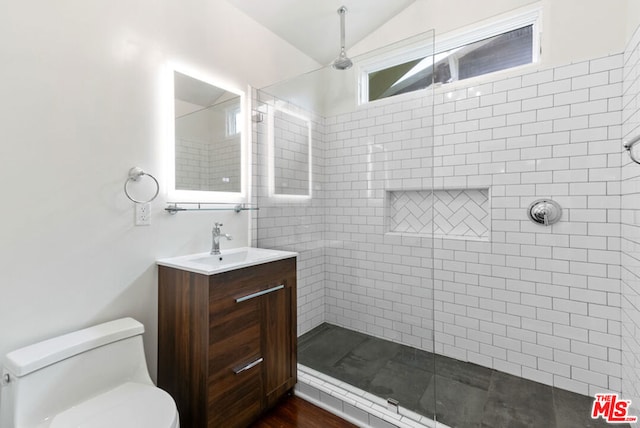 bathroom featuring toilet, vanity, a tile shower, and lofted ceiling