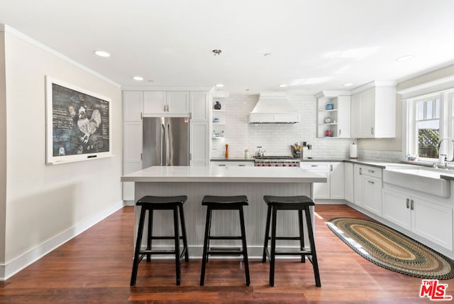 kitchen with white cabinetry, custom exhaust hood, stainless steel fridge, a center island, and sink