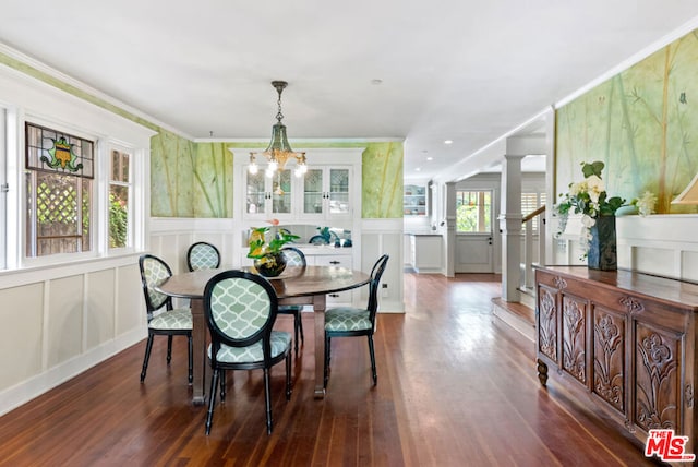 dining area featuring dark wood-type flooring, ornate columns, crown molding, and a notable chandelier