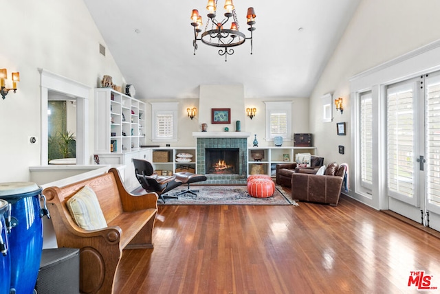 living room featuring wood-type flooring, vaulted ceiling, a tile fireplace, and a chandelier