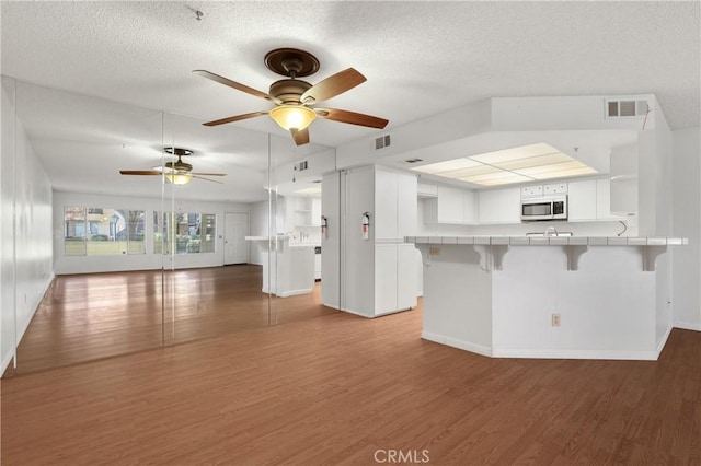 kitchen featuring kitchen peninsula, tile counters, dark wood-type flooring, white cabinets, and a breakfast bar