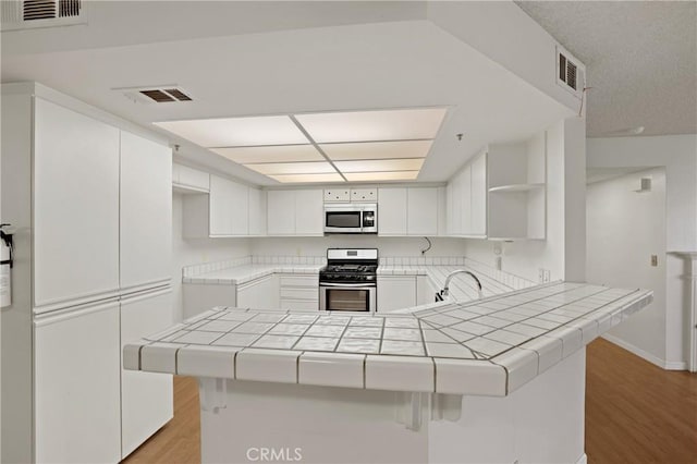 kitchen with tile counters, kitchen peninsula, and stainless steel appliances