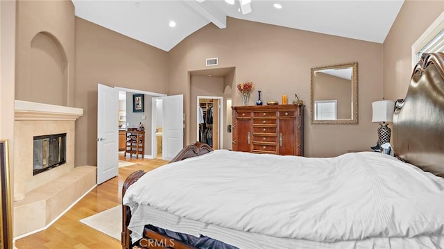 bedroom featuring light hardwood / wood-style floors, a tiled fireplace, a closet, vaulted ceiling with beams, and a walk in closet