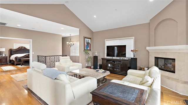 living room with a fireplace, light wood-type flooring, high vaulted ceiling, and an inviting chandelier