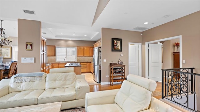 living room with a raised ceiling, sink, an inviting chandelier, and light hardwood / wood-style flooring