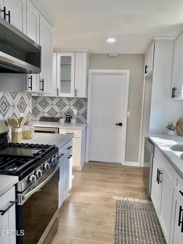 kitchen with white cabinets, backsplash, stainless steel appliances, and light hardwood / wood-style floors