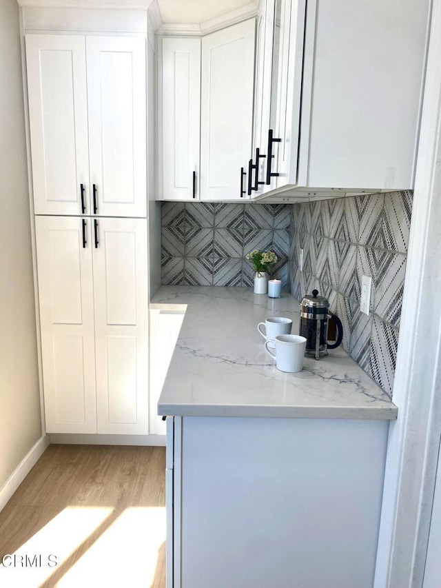 bar featuring white cabinets, light hardwood / wood-style floors, light stone countertops, and tasteful backsplash