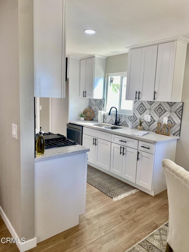 kitchen with sink, stainless steel gas cooktop, light hardwood / wood-style floors, decorative backsplash, and white cabinets