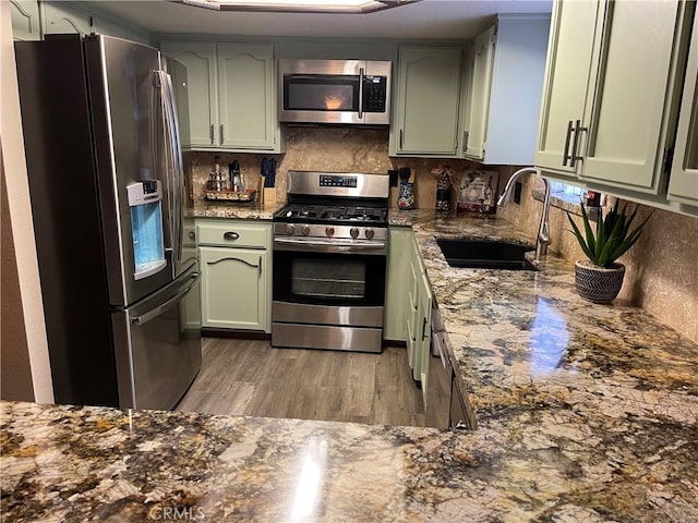 kitchen featuring appliances with stainless steel finishes, tasteful backsplash, sink, stone countertops, and green cabinets