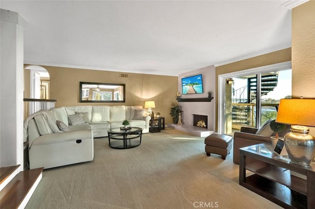 carpeted living room featuring arched walkways, a lit fireplace, ornamental molding, and visible vents