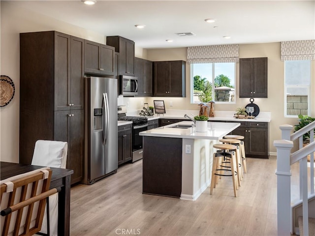 kitchen with stainless steel appliances, light hardwood / wood-style floors, a center island with sink, and a breakfast bar