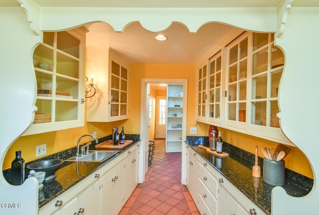 kitchen featuring dark stone countertops, sink, light tile patterned floors, and white cabinets