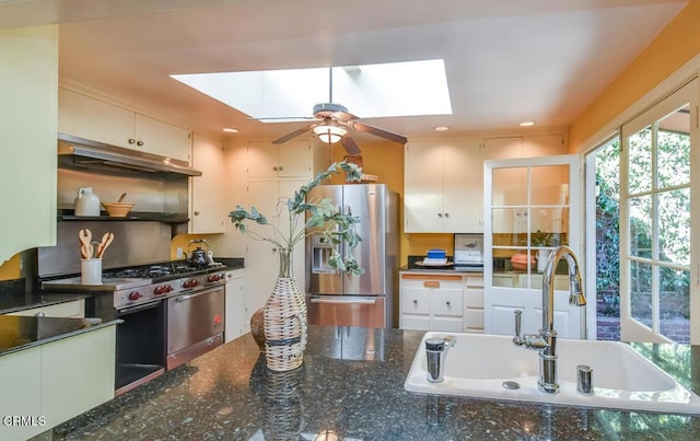 kitchen with appliances with stainless steel finishes, a skylight, sink, and white cabinets