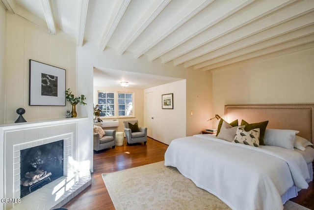 bedroom with a brick fireplace, beam ceiling, and dark wood-type flooring