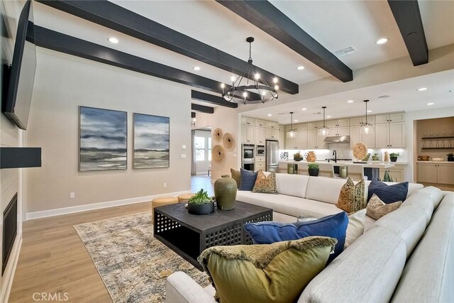 living room with beam ceiling, sink, a chandelier, and light hardwood / wood-style floors