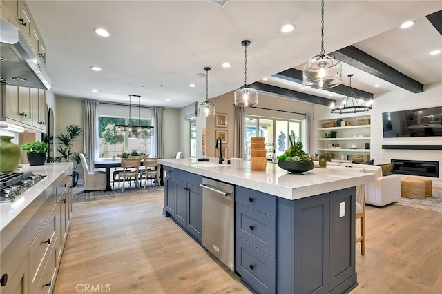 kitchen with a large island with sink, light hardwood / wood-style floors, hanging light fixtures, and appliances with stainless steel finishes