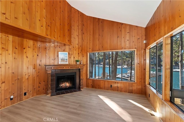 unfurnished living room with wood walls, a water view, hardwood / wood-style floors, and a tile fireplace