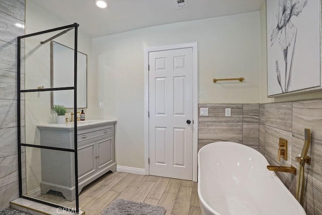 bathroom featuring separate shower and tub, vanity, and tile walls