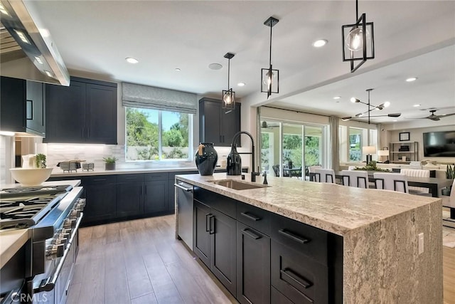 kitchen featuring decorative light fixtures, sink, ventilation hood, and a kitchen island with sink