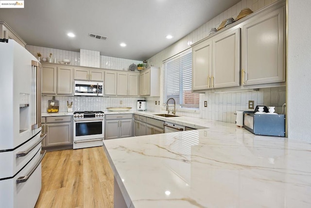 kitchen with range with gas cooktop, gray cabinetry, white fridge with ice dispenser, light stone countertops, and sink