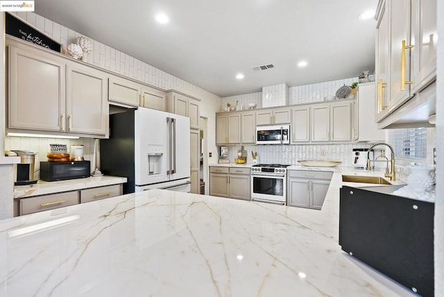 kitchen featuring gray cabinets, decorative backsplash, light stone countertops, high end appliances, and sink