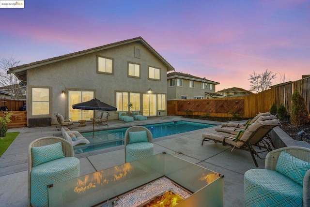 back house at dusk with a fenced in pool, a fire pit, and a patio