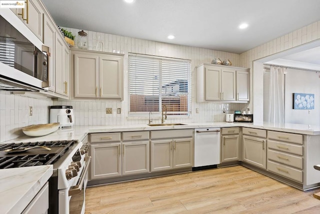 kitchen with light hardwood / wood-style floors, appliances with stainless steel finishes, backsplash, light stone counters, and sink