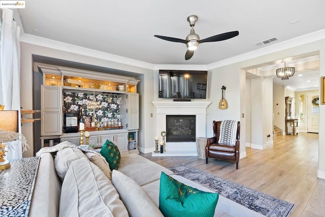 living room with crown molding, ceiling fan with notable chandelier, and light hardwood / wood-style floors