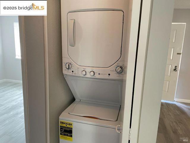 laundry room featuring stacked washer and clothes dryer and hardwood / wood-style flooring