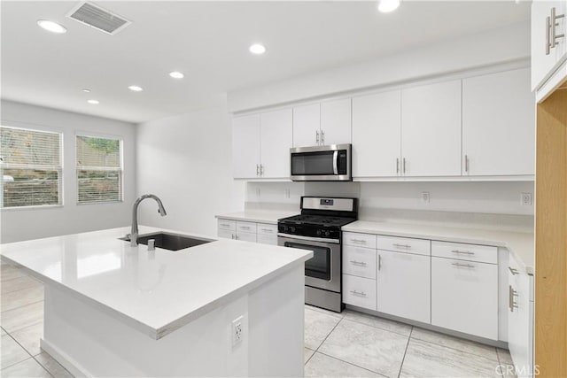 kitchen with sink, light tile patterned floors, appliances with stainless steel finishes, a kitchen island with sink, and white cabinets