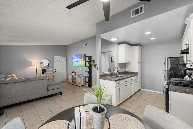 kitchen with black stove, sink, light tile patterned flooring, white cabinetry, and stainless steel fridge