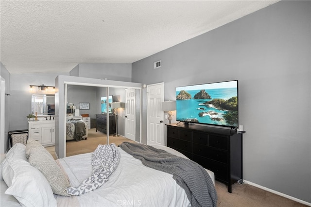 bedroom with a textured ceiling, vaulted ceiling, light colored carpet, ensuite bathroom, and multiple closets